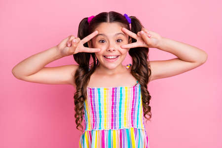 Photo of beautiful little lady two lovely cute curly tails showing v-sign symbols near eyes good mood wear colored summer dress isolated pastel pink color backgroundの写真素材
