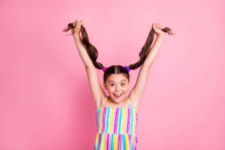 Photo of pretty beautiful little lady raise hold hands two cute curly tails up showing long length new shampoo effect wear colored summer dress isolated pastel pink color backgroundの写真素材