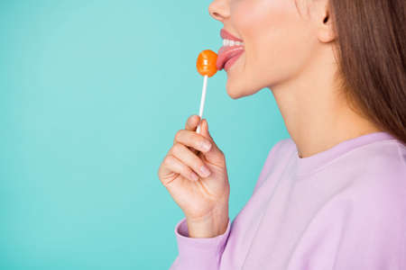 Cropped profile photo of funny lady hold lollipop hand sweets addicted person lick tasty candy tongue wear violet sweater isolated vibrant teal color backgroundの写真素材