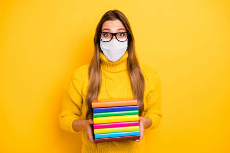 Portrait of nice healthy stunned girl nerd wearing safety mask holding in hands pile book learn...