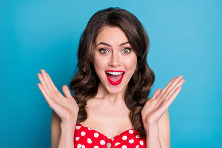 Closeup photo of pretty funny wavy lady raise arms up open mouth excited listen good news overjoyed expression wear red dotted dress singlet isolated blue color backgroundの写真素材