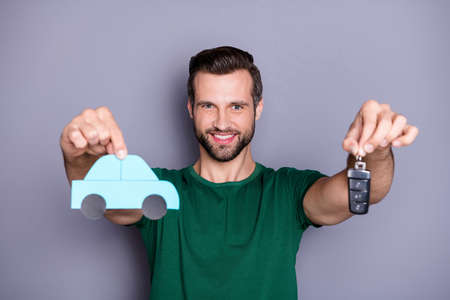 Portrait of positive cheerful guy hold paper card car present keys new transport purchase for easy traveling tourism wear green t-shirt isolated over gray color backgroundの写真素材