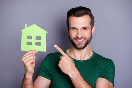 Portrait of positive confident real estate agent man hold paper card house point index finger suggest select rent mortgage wear green t-shirt isolated over gray color backgroundの写真素材