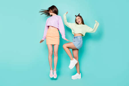Full length body size of two nice attractive slim fit girlish cheerful cheery girls having fun jumping dancing fooling isolated over bright vivid shine vibrant blue green turquoise color backgroundの写真素材
