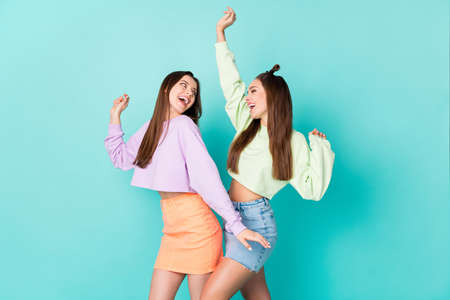 Photo of two cheerful lady girlfriends celebrate student party cool clothes dance favorite song wear cropped sweaters naked belly short skirts isolated pastel teal color backgroundの写真素材