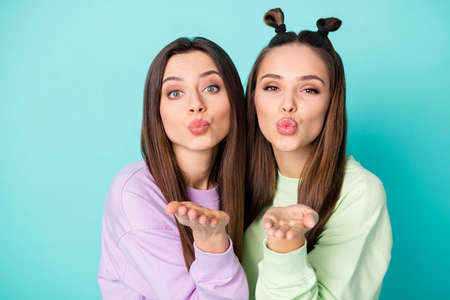 Closeup photo of two beautiful brunet lady friends hold open arms sending handsome guys air kisses wear green violet youngster sweaters isolated pastel teal color backgroundの写真素材