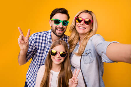 Closeup photo of mommy lady cool daddy little daughter spend quarantine together make showing v-sign symbols trendy family wear sun specs casual shirts isolated yellow color backgroundの写真素材