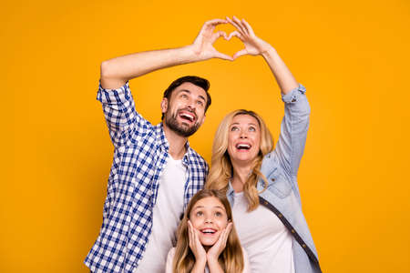 Photo beautiful mom lady handsome dad little school girl daughter enjoy happy parents celebrate anniversary make heart figure fingers wear casual clothes isolated yellow color backgroundの写真素材