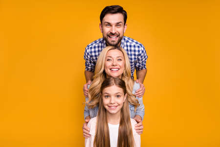 Photo beautiful mom lady handsome husband dad couple little school girl daughter standing in order hugging good mood offspring wear casual clothes isolated yellow color backgroundの写真素材