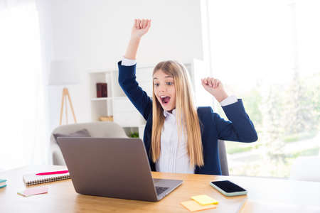 Photo of little blond pupil student girl notebook table chatting online lesson call raise fists glad...