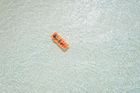 Top above high angle aerial drone view of her she attractive girl floating on rubber mattress in clean clear perfect gray ocean water enjoying, sunny weather spending weekend hot tourの写真素材