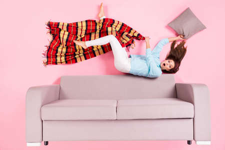 attractive stunned confused girl lying on divan checkered plaid bedtime regime isolated over pink pastel color backgroundの写真素材