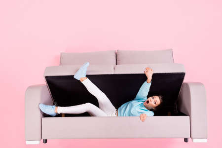 helpless worried girl lying inside divan trying to get out isolated over pink pastel color...