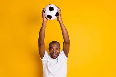 Delighted positive cheerful afro american guy hold football ball celebrateの写真素材