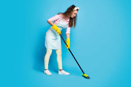 Full length body size profile side view of her she nice attractive focused hardworking maid sweeping floor after cooking dinner food cleanup isolated bright vivid shine vibrant blue color backgroundの写真素材