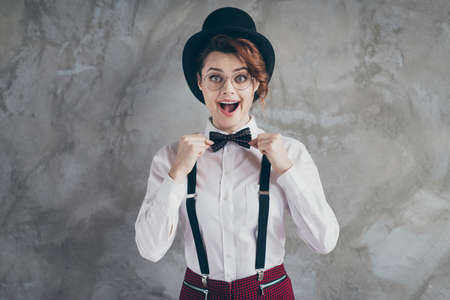 Portrait of nice-looking attractive lovely fashionable classy cheerful cheery glad wavy-haired girl fixing bow tie preparing isolated on gray concrete industrial wall backgroundの写真素材