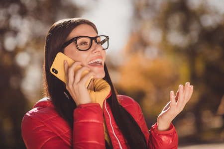 Close up photo of positive cheerful girl rest relax fall town center park call smartphone tell say millennial news wear red outerwearの写真素材