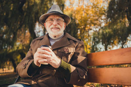 Photo of inspired old man sit bench drink hold takeout coffee mug dream sunny yellow colorful...