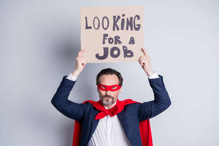 Looking for a job. Photo of stressed mature business guy homeless person career crash super hero costume carton placard seek work wear suit red face mask cloak isolated grey backgroundの写真素材