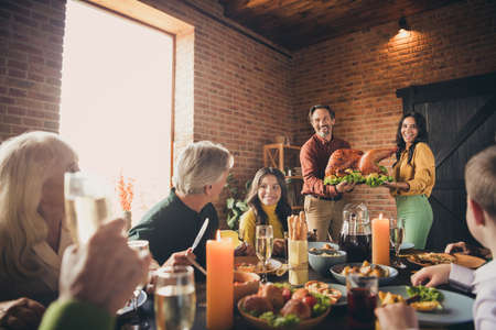 Portrait of nice attractive cheerful family brother sister gathering wife husband carrying plate fresh homemade domestic turkey serving table festive at modern loft industrial brick interior houseの写真素材