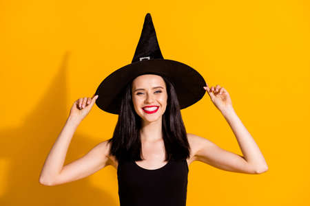 Photo of pretty charming young magician lady toothy beaming smile hold cap role play october event evening wear black wizard headwear dress isolated bright yellow color backgroundの写真素材