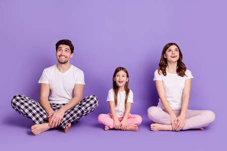 Portrait of cheerful glad family dad mom offspring daughter wearing cozy cotton pajama sitting on...