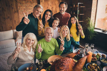 Portrait of nice attractive cheerful positive family grandparents parents grandchildren brother sister embracing showing v-sign celebratory harvest at modern loft brick industrial interiorの写真素材