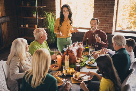 Portrait of nice attractive cheerful family friends friendship parents meeting eating festal luncheon turkey drinking champagne mom saying toast at modern loft brick industrial interiorの写真素材