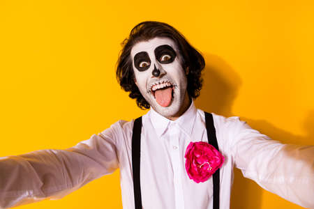 Self-portrait of his he nice handsome spooky baleful cheerful cheery foolish guy catrina celebratory having fun showing tongue out fooling isolated bright vivid shine vibrant yellow color backgroundの写真素材