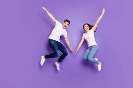 Full length photo of cheerful married couple man woman jump enjoy leisure free time rest wear casual style clothes sneakers isolated over violet color backgroundの写真素材