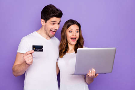 Photo pretty lady handsome guy couple hold notebook spend free time together use plastic wireless credit card online transfer buy delivery food wear t-shirts isolated purple color backgroundの写真素材