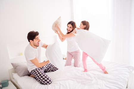 Photo of happy cool young family mommy daddy daughter bed sheets good mood spend together quarantine weekend playing games pillow fighting self isolation bedroom indoorsの写真素材