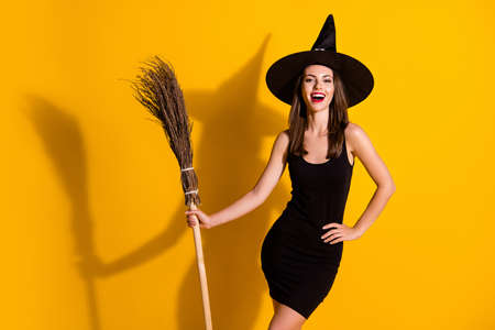 Portrait of her she nice-looking attractive pretty charming lovely slender cheerful cheery lady wizard holding in hand broom festal event isolated bright vivid shine vibrant yellow color backgroundの写真素材