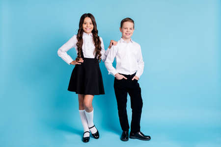 Full body size photo of two girl boy model schoolchildren smiling hands pockets cuddle a-students wear uniform white shirt black pants dress shoes isolated blue color backgroundの写真素材