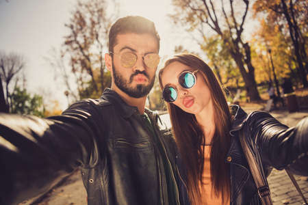 Portrait of romance couple make selfie in yellow october sunshine trees park send air kiss wear sunglass jacketの写真素材