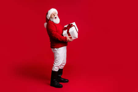Full length profile side photo amazed old man santa claus headwear hold big gift box get x-mas jolly holly tradition event wear trousers boots jumper isolated bright shine color backgroundの写真素材