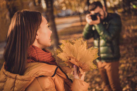 Back rear spine view photo of girl model hold september maple leaves pose for photographer guy shoot camera in autumn parkの写真素材