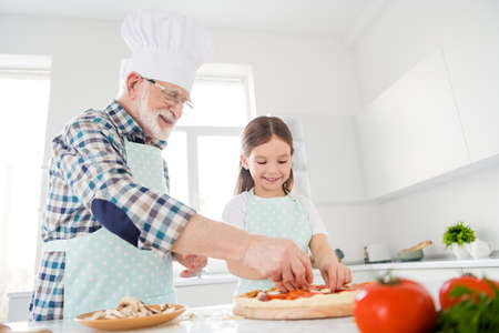 Photo of little girl granddaughter aged granddad assist put fresh cut ingredients on dough family pizza recipe finishing decoration cooking together friends weekend home kitchen indoorsの写真素材