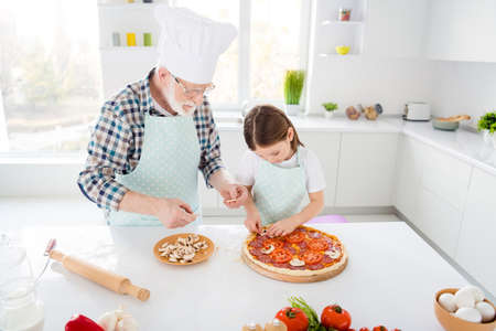 Portrait of his he her she focused grey-haired grandparent grandchild teaching cook homemade vegs vegetarian pizza mushroom workshop support in light white interior kitchen houseの写真素材