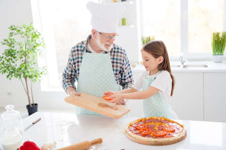 Photo of little girl granddaughter spend time aged granddad assistance put fresh cut ingredients on dough family pizza recipe cooking together friends weekend home kitchen indoorsの写真素材