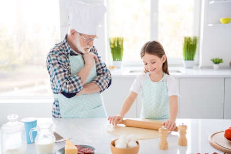 Photo of little girl granddaughter passing examination aged chef grandpa looking attentively forming dough rolling pin baking cookies weekend home kitchen indoorsの写真素材