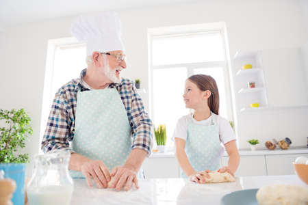 Photo of little girl granddaughter help aged grandpa mixing forming dough baking cookies together best friends leisure activity weekend home kitchen indoorsの写真素材