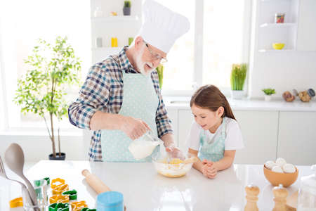 Photo of little girl granddaughter watch interested aged grandpa mixing dough in plate add milk baking cake cookies together old chef lesson weekend home kitchen indoorsの写真素材
