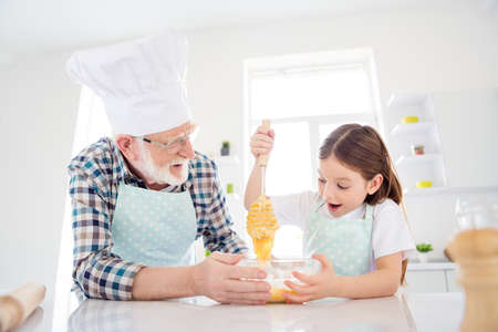 Close-up portrait of nice cheerful cheery glad grey-haired grandpa grandchild cooking domestic homemade tasty yummy dough cookies having fun leisure in modern light white interior kitchen houseの写真素材