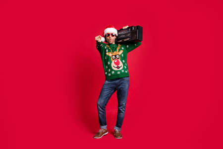 Full length body size view of attractive funny cool hipster guy wearing Santa hat carrying boombox...