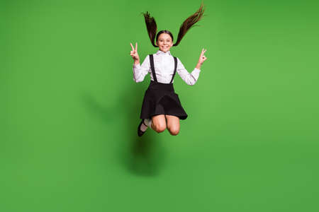 Photo portrait of brunette schoolgirl with pigtails jumping up holding two v-signs isolated on vivid...