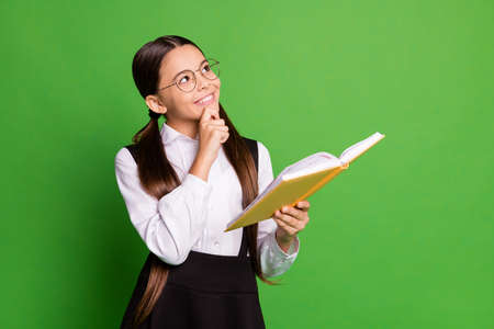 Photo portrait of clever girl wearing glasses holding yellow book in one hand touching chin with...