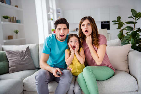 Photo of shocked terrified three people mommy daddy small child girl sit cozy couch remote control switch channel search cartoons find horror scream in house indoorsの写真素材