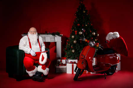 Full length photo of santa claus sit in cozy chair house concept with evergreen tree fireplace tradition x-mas decoration isolated bright color backgroundの写真素材