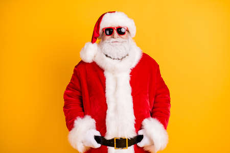 Portrait of nice funny fashionable confident white-haired Santa holding belt wearing December fluffy look outfit isolated bright vivid shine vibrant yellow color backgroundの写真素材